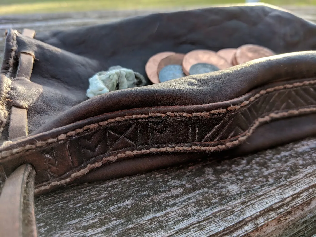 The open purse showing coins and rough stones, its tooled border on weathered wood