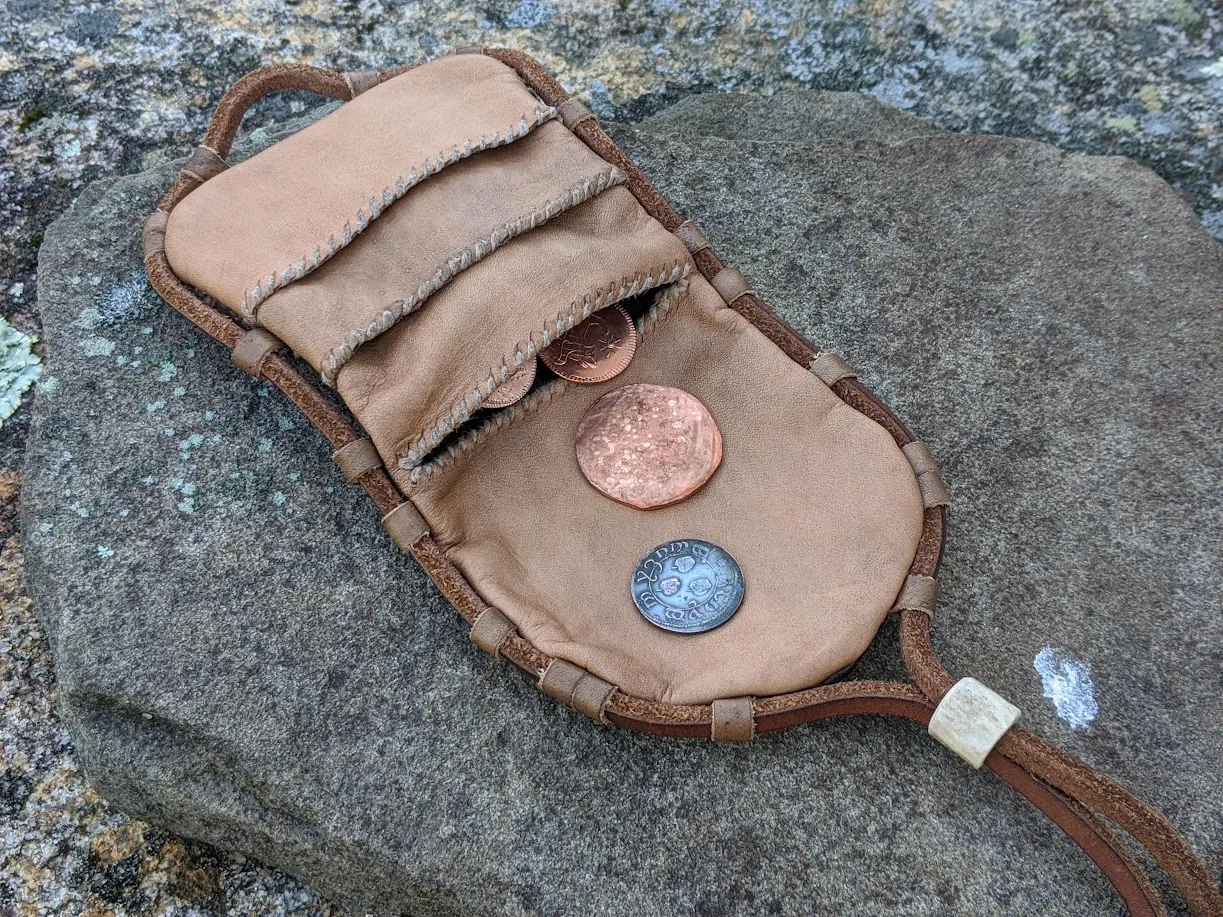 The leather wallet opened flat on stone, coins in its pocket