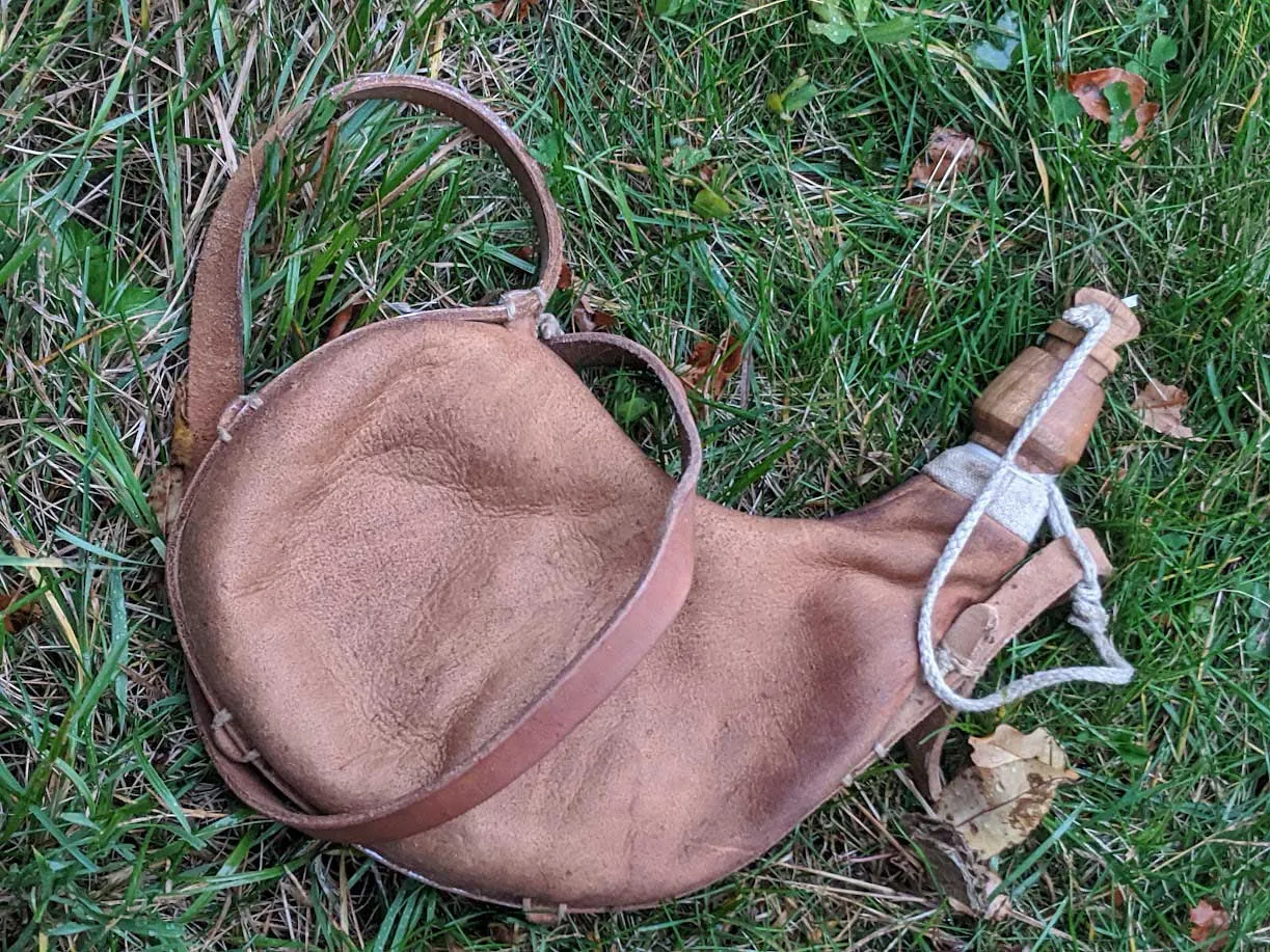 A leather waterskin with a wooden spout, lying in grass